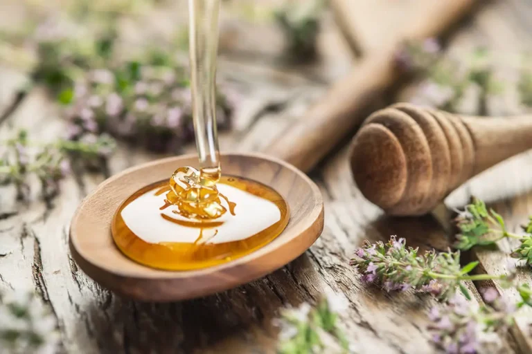 Wooden spoon full of honey with sprigs of thyme on a wooden table