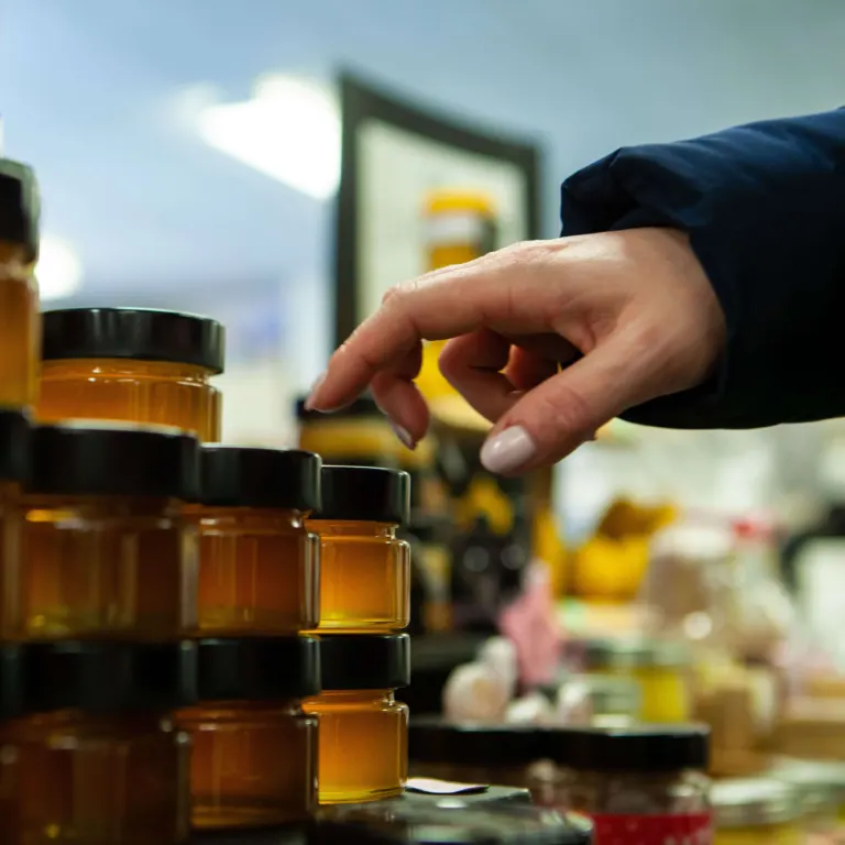 Hand choosing a jar of honey from a stall