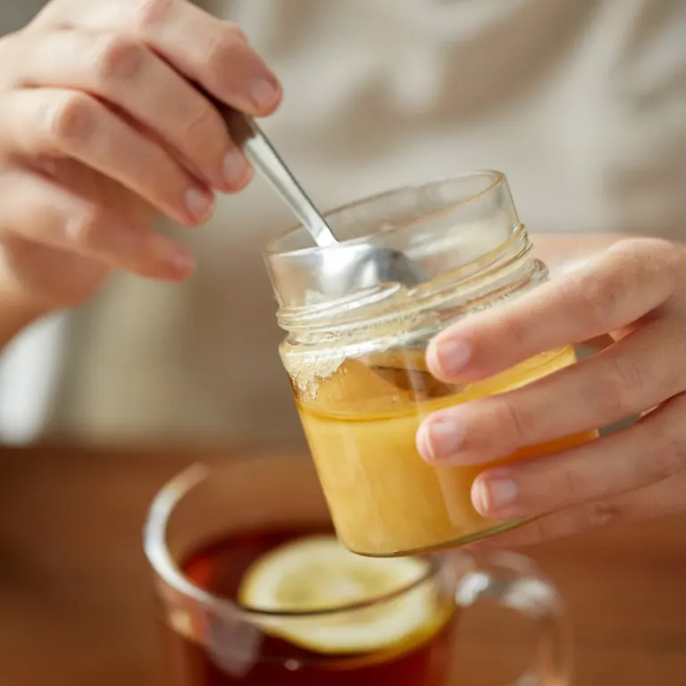 Hands holding a jar of honey with a spoon over a lemon tea