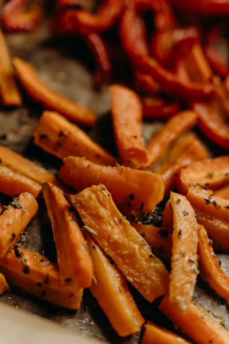 Bâtonnets de carottes rôties au miel, herbes et graines sur une plaque de cuisson, quelques lanières de poivron rouge