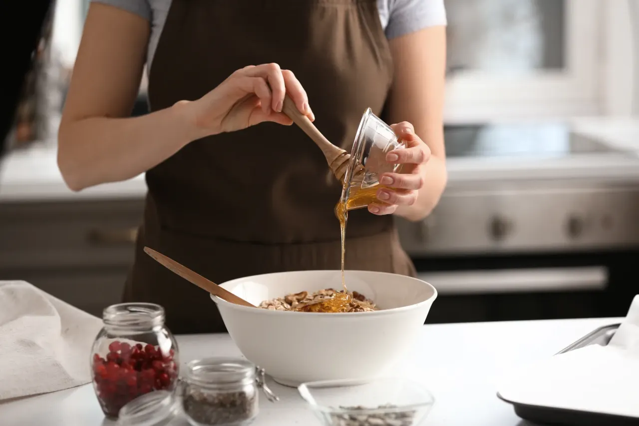 Miel versé d'un petit pot dans un grand bol de flocons d'avoine et de fruits secs, cranberries et graines en bocaux