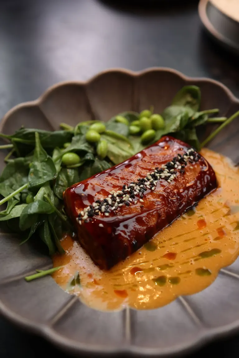 Pavé de saumon laqué au miel et au soja, parsemé de sésame, sur épinards et edamame dans une assiette grise