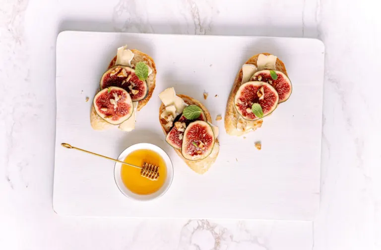 Trois toasts de chèvre frais et figues coupées en deux, près d'un bol de miel et d'une cuillère à miel